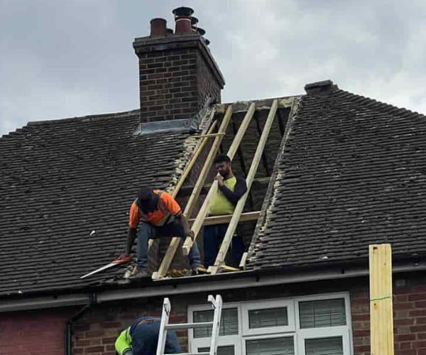 This is a photo of a roof repair being carried out. A section of the roof has been stripped and two roofers are replacing the rafters. Works being carried out by WDF Roofing St Neots